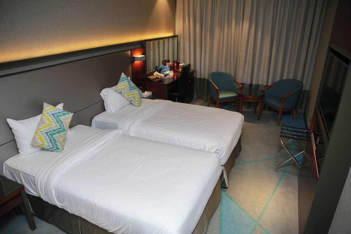 A hotel room with two beds, a desk, and a chair.