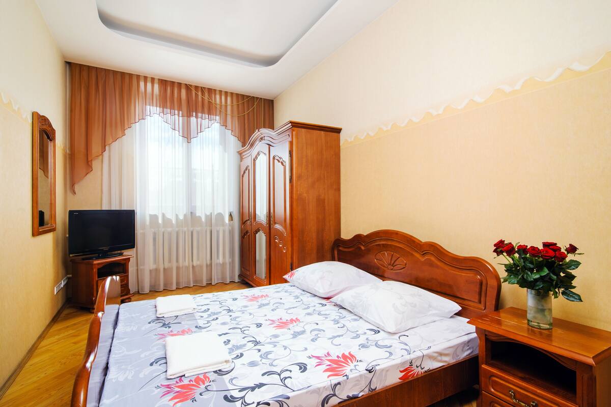 Ein Hotelzimmer mit einem hölzernen Bett, einem Fernseher, einem Kleiderschrank und einer Vase mit Blumen.
