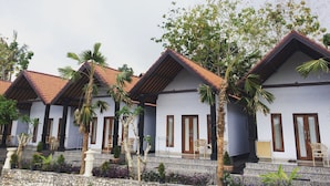 A row of white buildings with red-tiled roofs and wooden doors, surrounded by palm trees and potted plants.