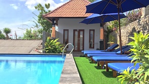 A swimming pool with blue lounge chairs and umbrellas, surrounded by greenery and a stone wall.