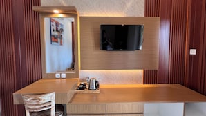 A modern hotel room with a wooden desk, a mounted flat-screen TV, a mirror, and a chair.