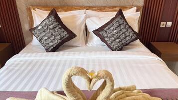 A neatly made bed with white linens, two decorative pillows with a leaf pattern, and two towels arranged in a heart shape with flowers.