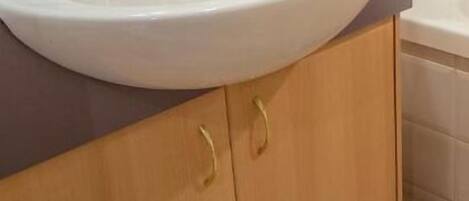 Een badkamer met een wit wastafelmeubel, houten kastjes en een betegelde vloer.