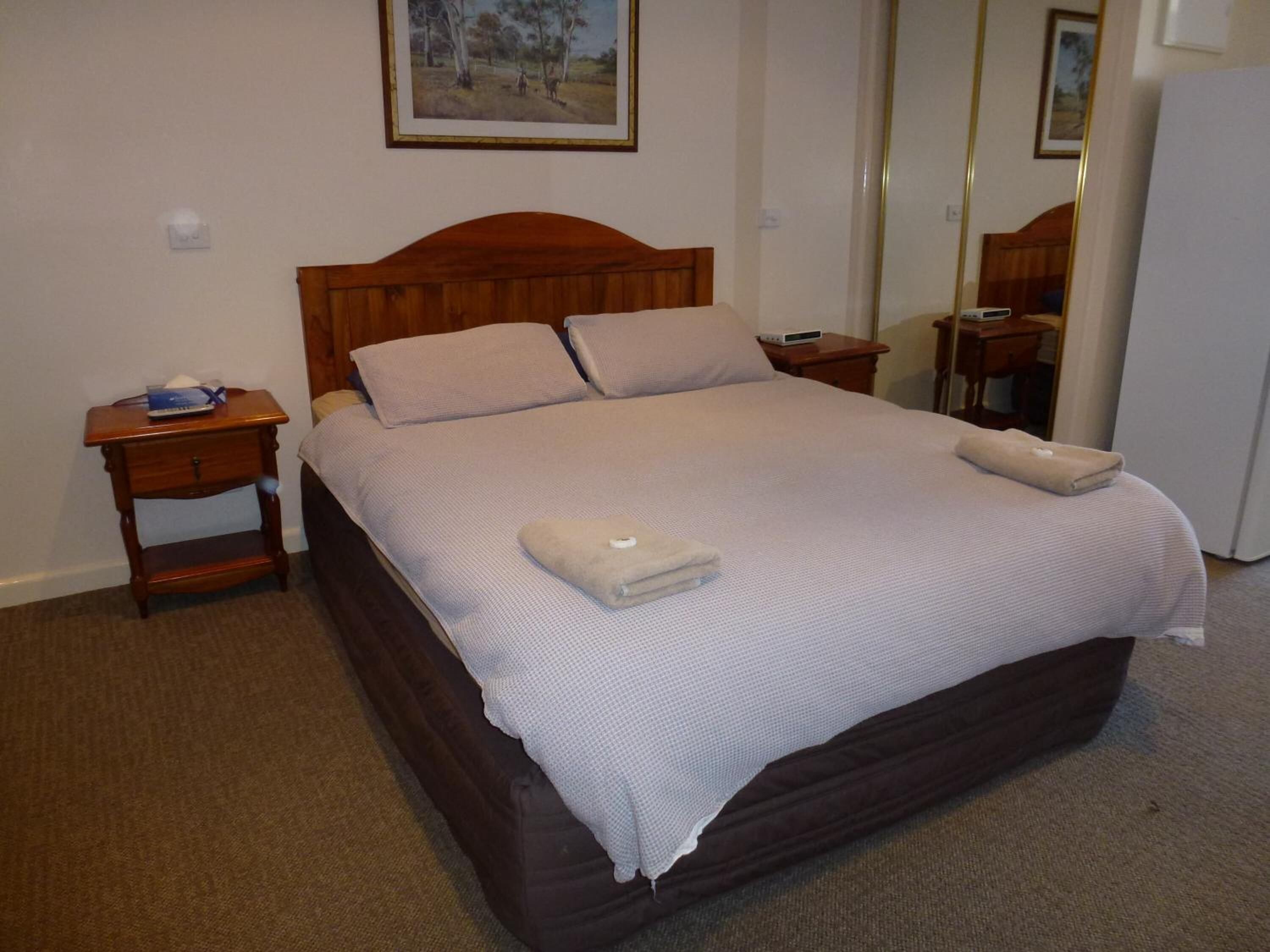 A neatly made bed with a wooden headboard, a bedside table with a lamp, and a mirror on the wall.