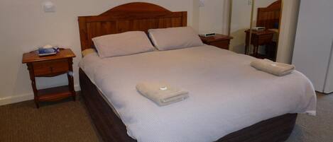 A neatly made bed with a wooden headboard, a bedside table with a lamp, and a mirror on the wall.