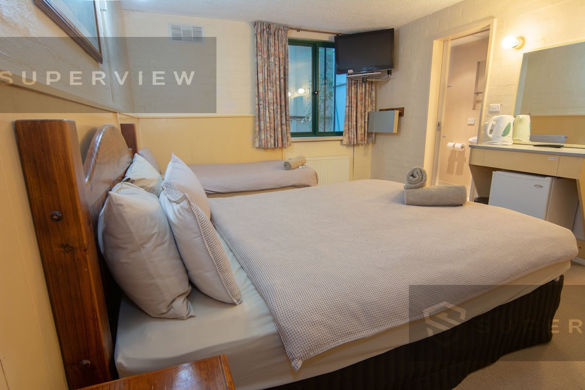 A hotel room with a bed, a small desk with a mirror, a television mounted on the wall, and a window with curtains.