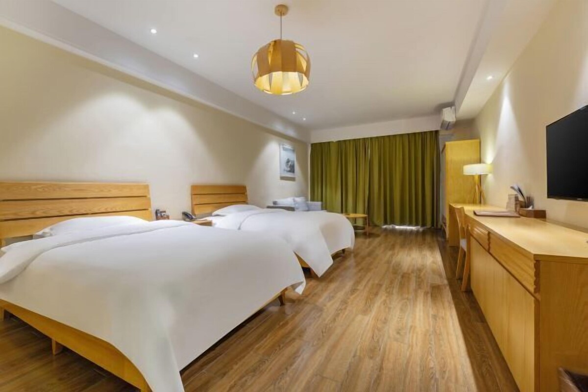 A hotel room with two beds, a wooden desk, a television, and a green curtain.