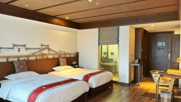 Een hotelkamer met twee bedden, houten vloeren, een groot raam en uitzicht op traditionele gebouwen.