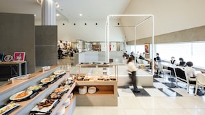 Une cafétéria moderne proposant une grande variété de plats présentés sur des comptoirs, avec un espace de service central et un coin repas équipé de tables et de chaises.