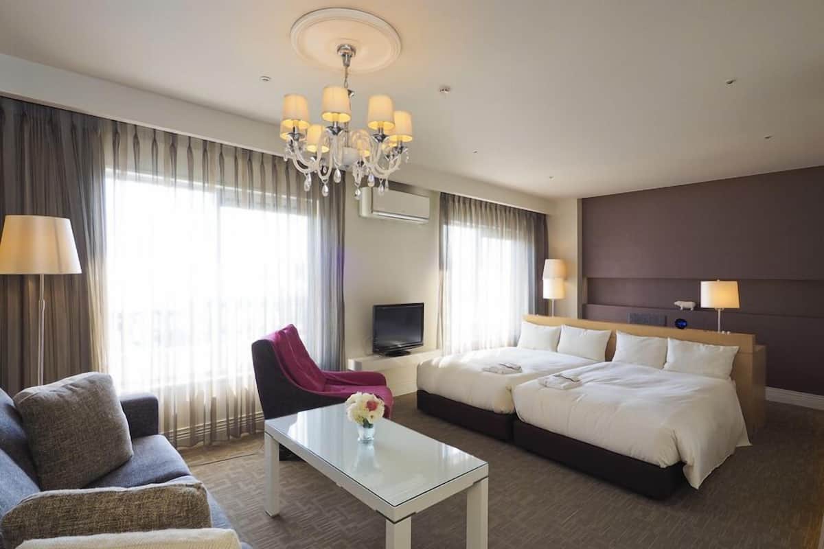 Een hotelkamer met een bed, twee nachtkastjes, een bank, een stoel, een televisie en een kroonluchter.