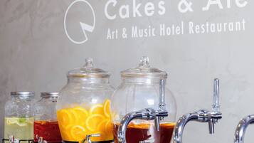 Una estación de bebidas con tres frascos de vidrio que contienen diferentes bebidas, un grifo y un letrero que dice 'Cakes & Ale Art & Music Hotel Restaurant'.