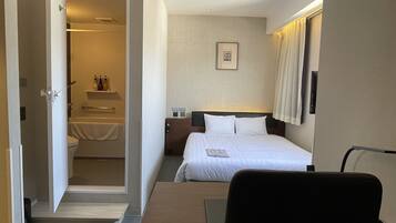 Ein Hotelzimmer mit Bett, Schreibtisch, Stuhl, Nachttisch, einem Bild an der Wand und einem durchgegangenen Tür erkennbaren Badezimmer.