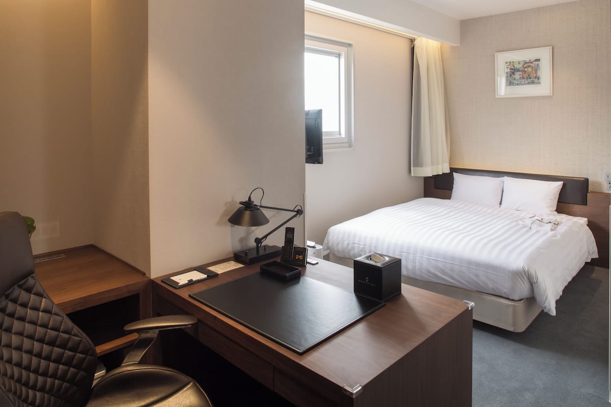 Een hotelkamer met een bureau, stoel, bed en raam met gordijnen.