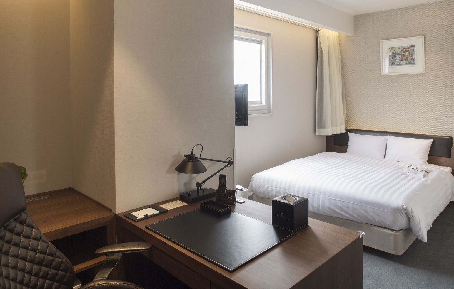 Une chambre d’hôtel équipée d’un bureau, d’une chaise, d’un lit et d’une fenêtre.