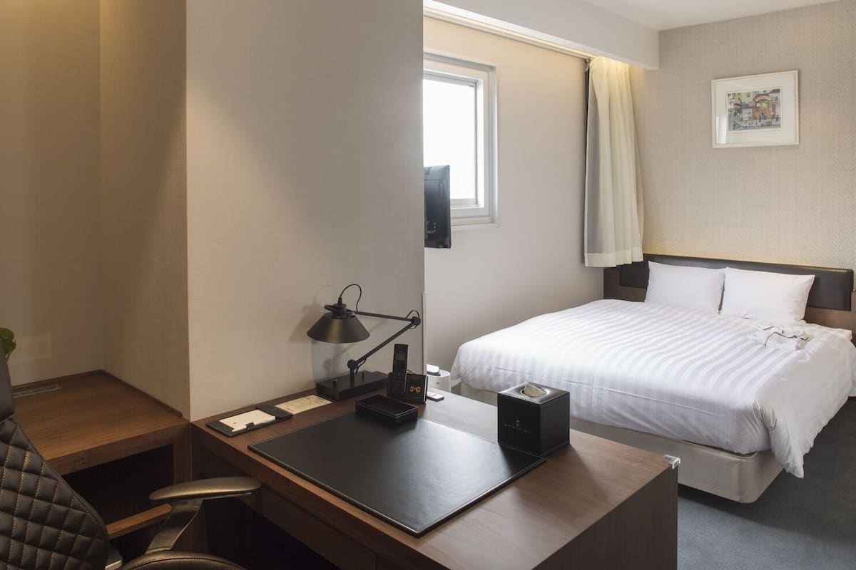 Een hotelkamer met een bureau, stoel, bed en een raam.