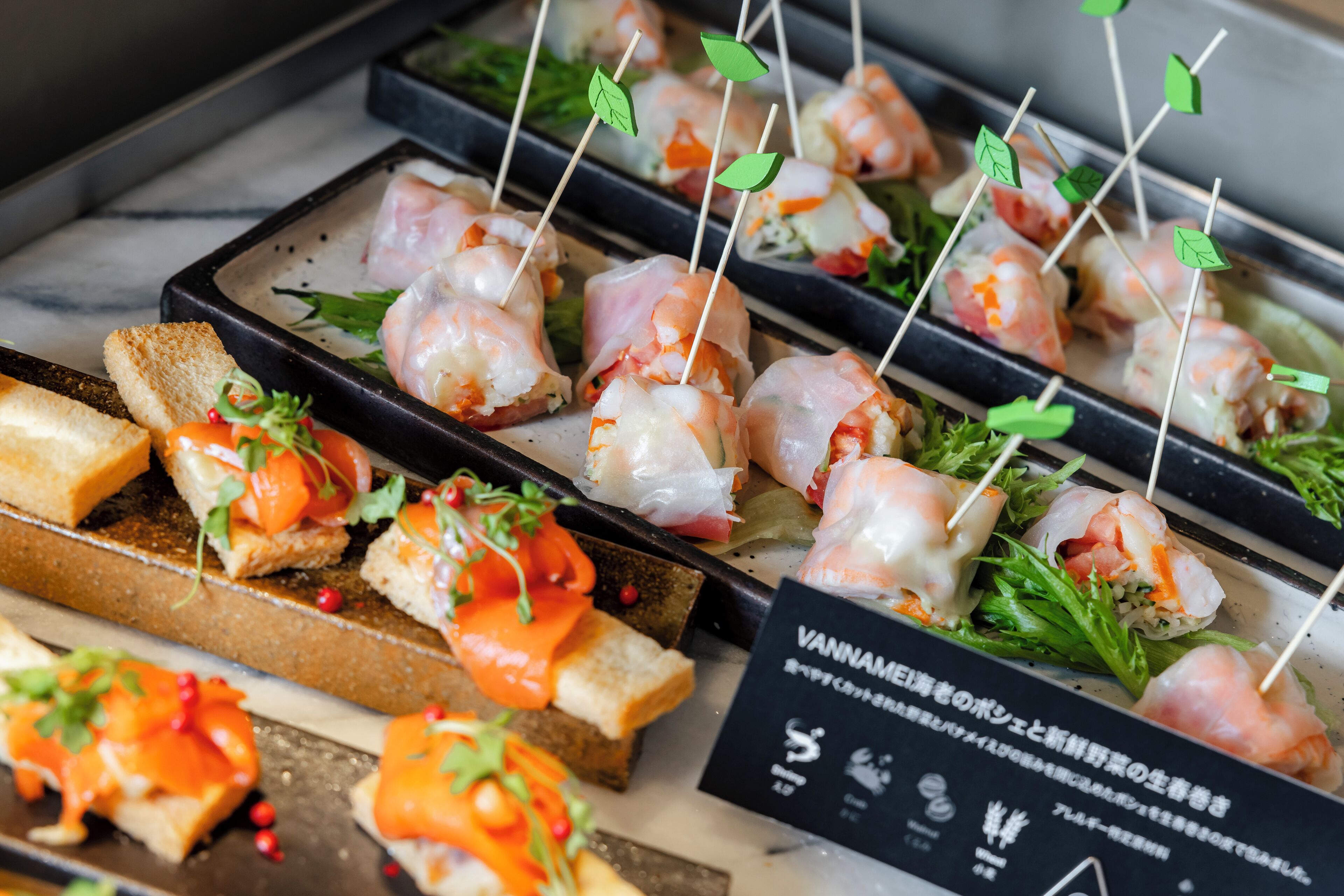 Une variété d’amuse-gueules, notamment des brochettes de crevettes et des sandwichs, présentés sur un plateau.
