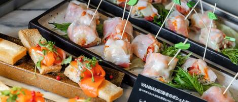Une variété d’amuse-gueules, notamment des brochettes de crevettes et des sandwichs, présentés sur un plateau.