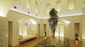 Un hall d’entrée spacieux avec un espace salon central, une grande plante en pot et un sol à motifs.