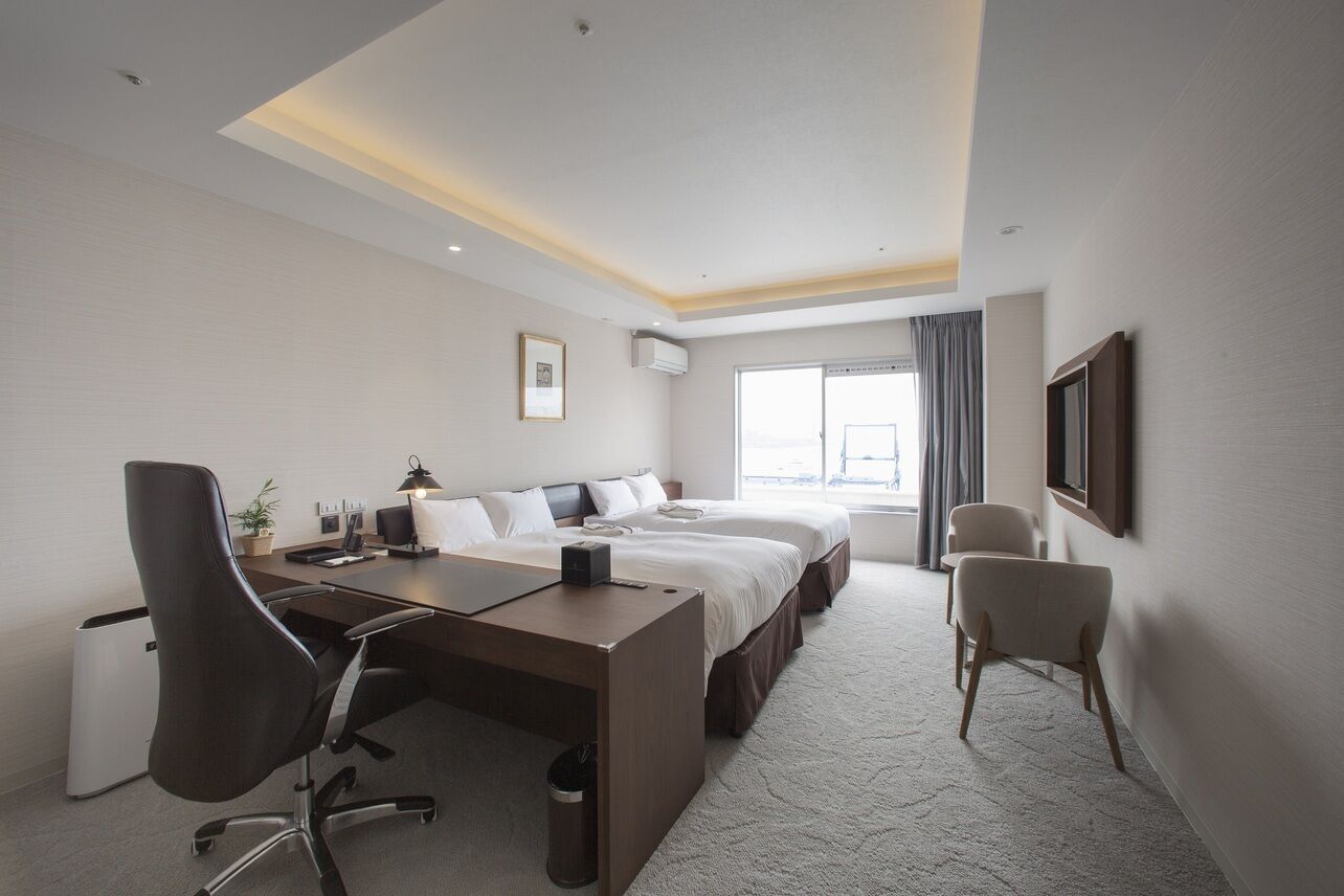 Une chambre d’hôtel avec un lit, un bureau, une chaise et une grande fenêtre.