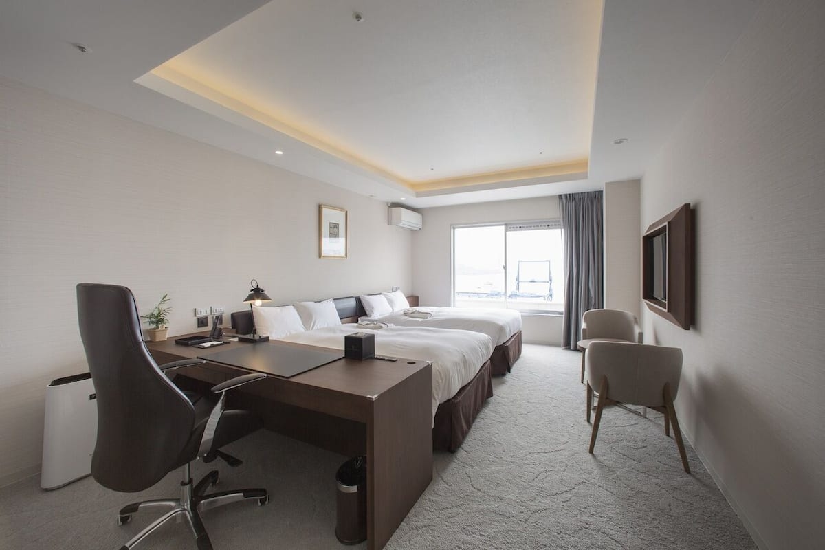 Een hotelkamer met een bed, bureau, stoel en een groot raam.
