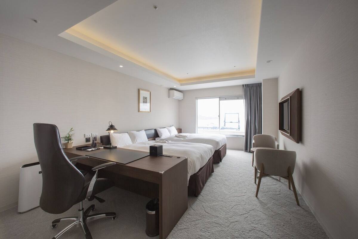 Une chambre d’hôtel avec un lit, un bureau, une chaise et une grande fenêtre.