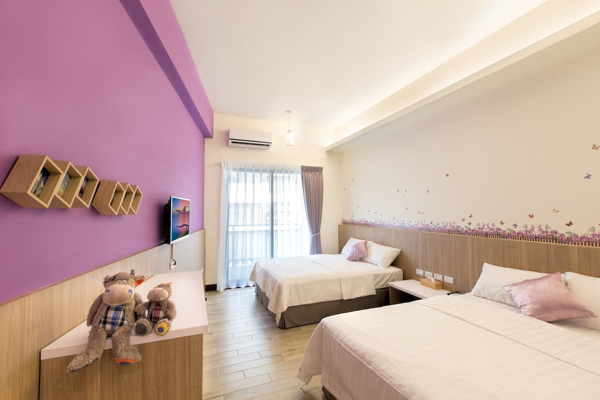 A hotel room with two beds, a wooden desk, and a wall-mounted TV.