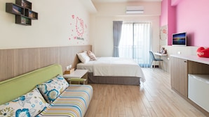 Une chambre d’hôtel moderne équipée d’un lit, d’un bureau, d’une petite kitchenette et d’un coin salon avec un canapé.