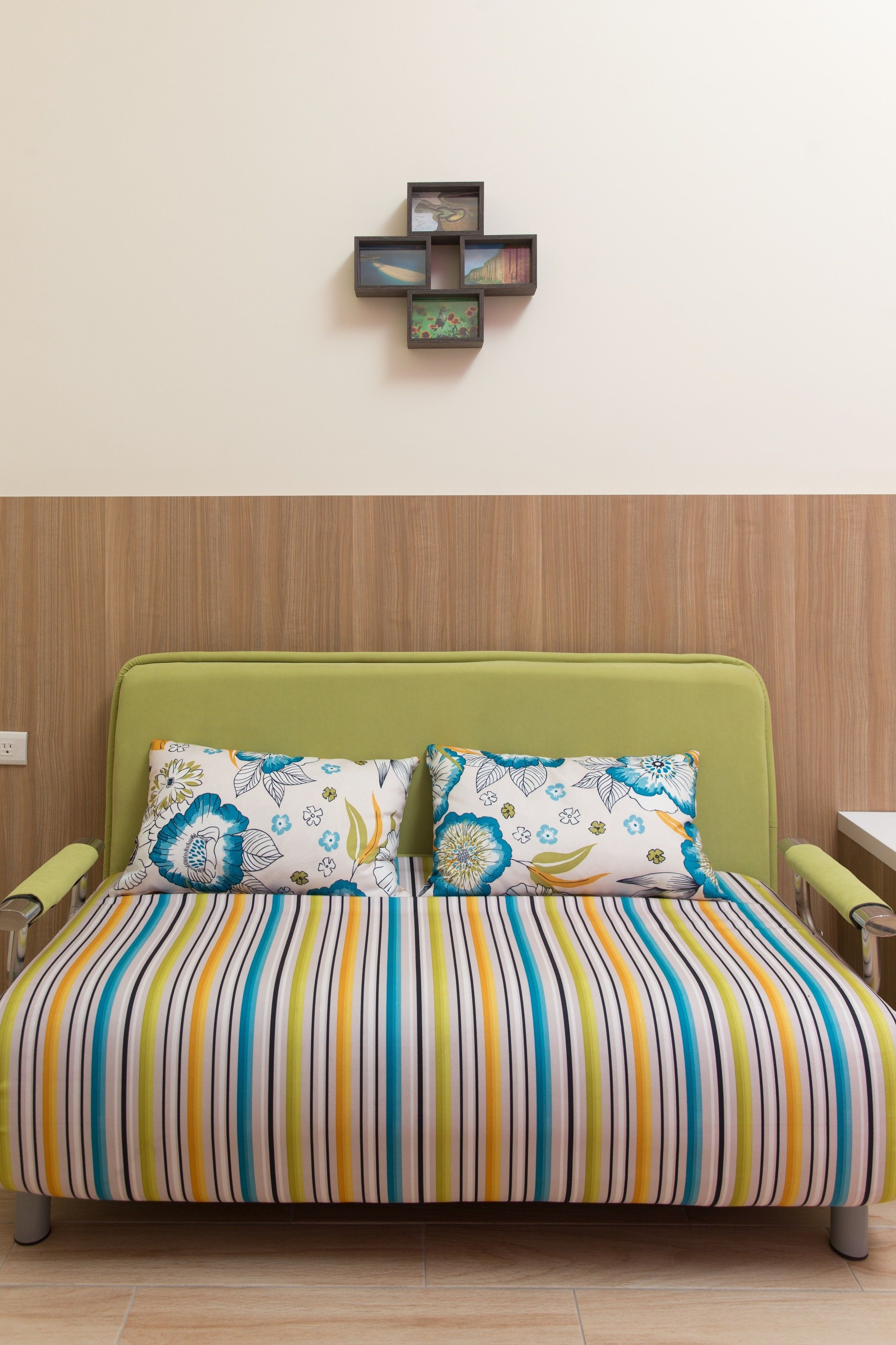 Una habitación con un sofá cama verde, dos almohadas estampadas y un cuadro colgado en la pared.
