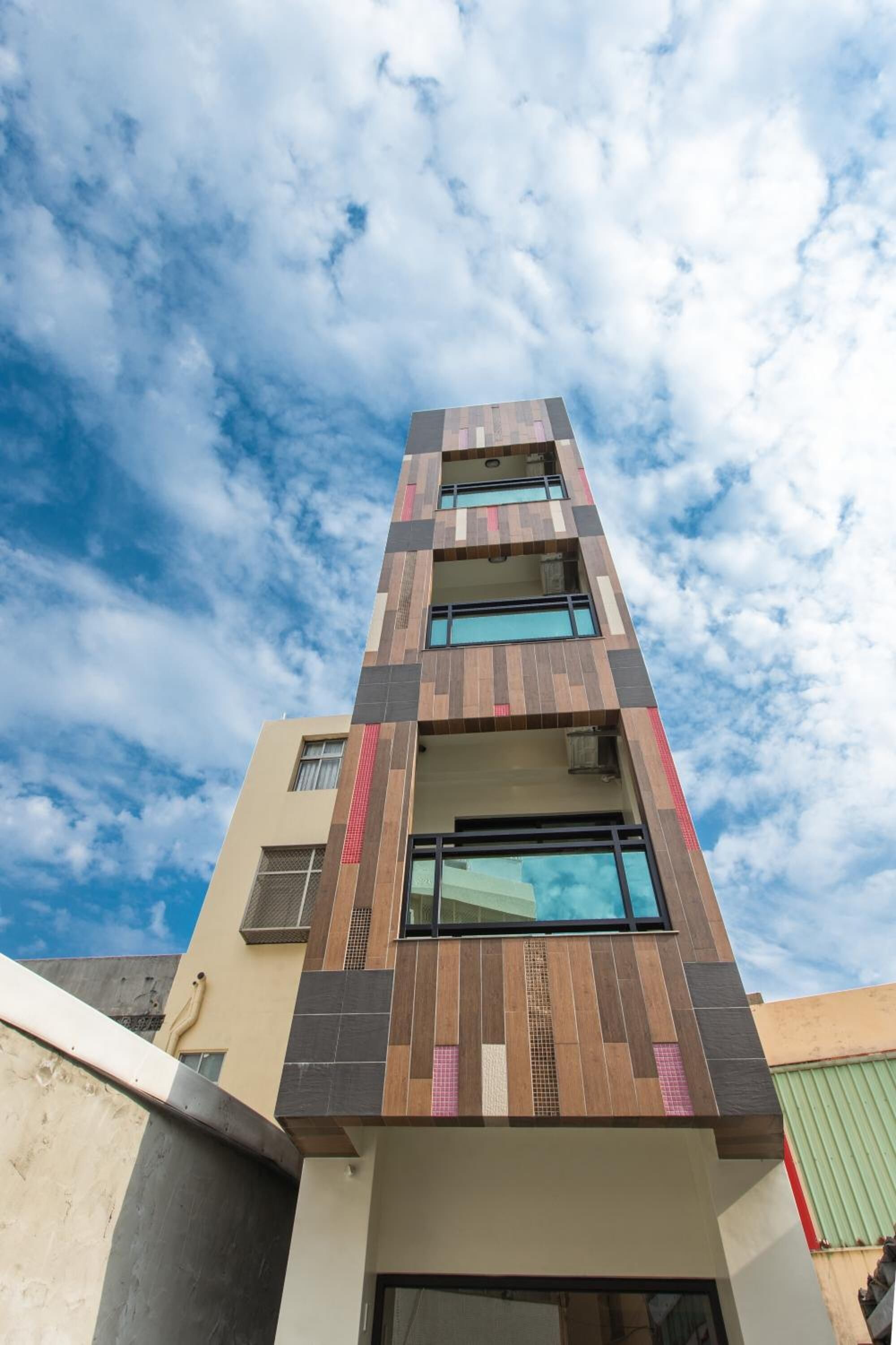 A modern multi-story building with a mix of wood and stone facade, large windows, and a clear sky.