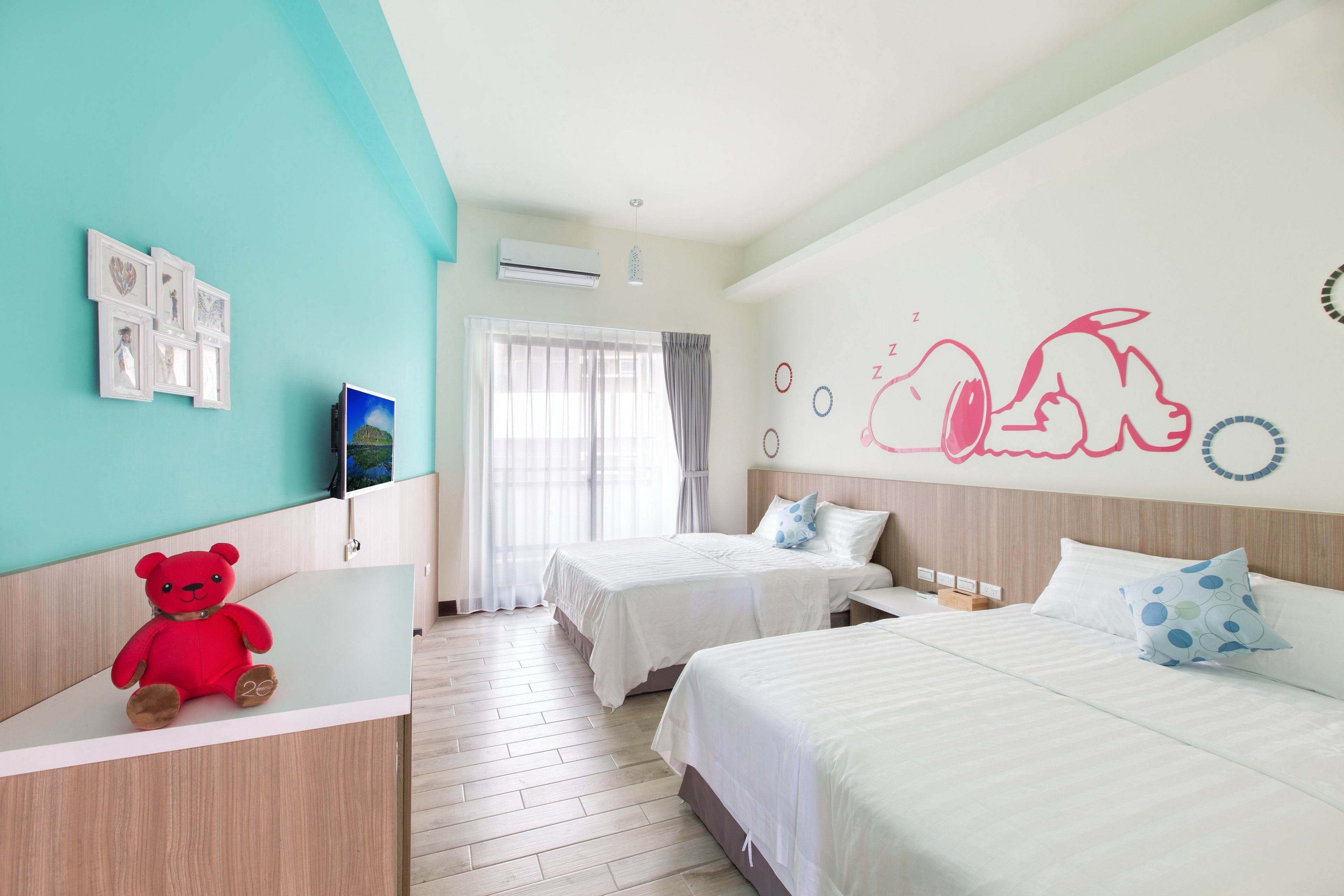 A hotel room with two beds, a red teddy bear on a counter, and a wall with a bear illustration.