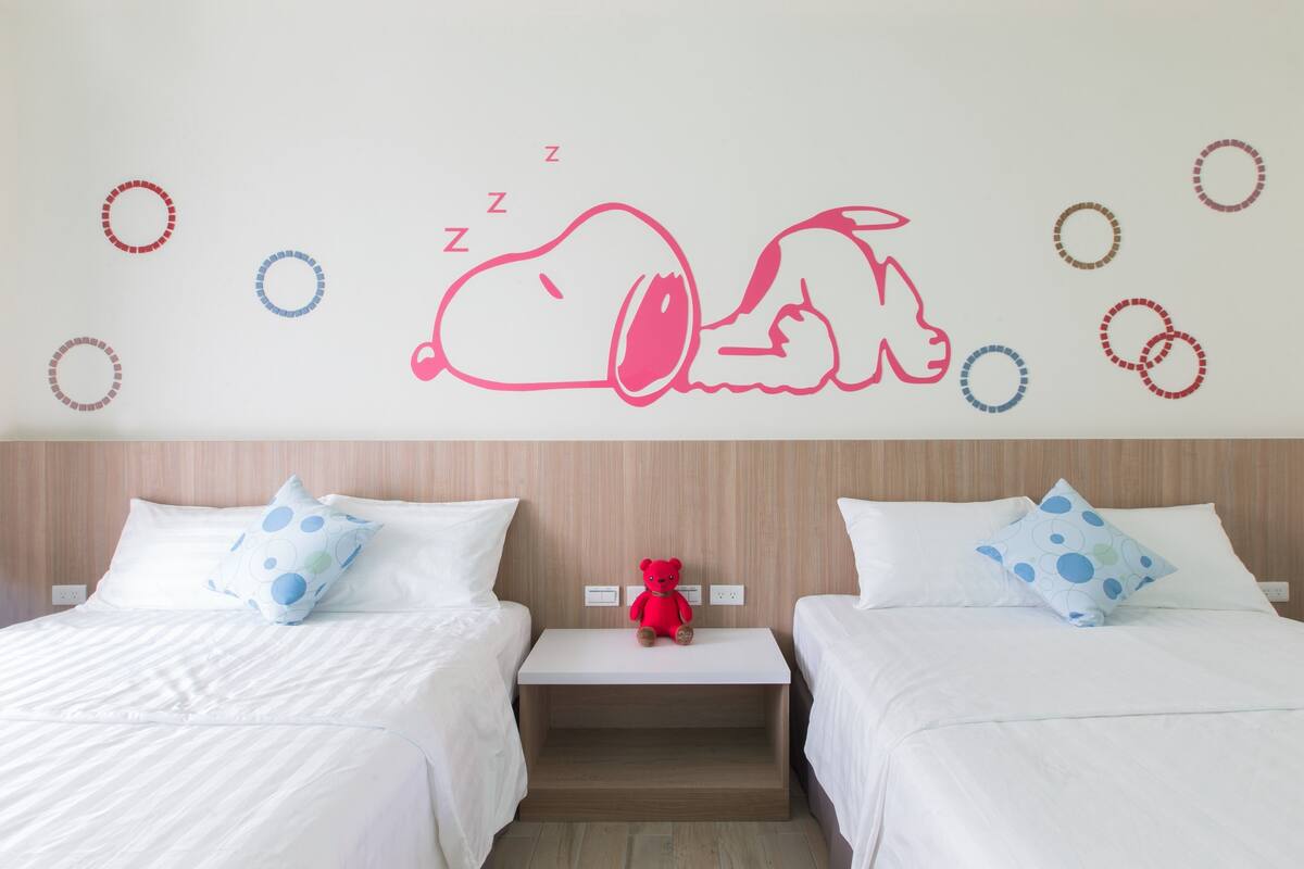 A hotel room with two beds, each with a pillow and a bedside table.