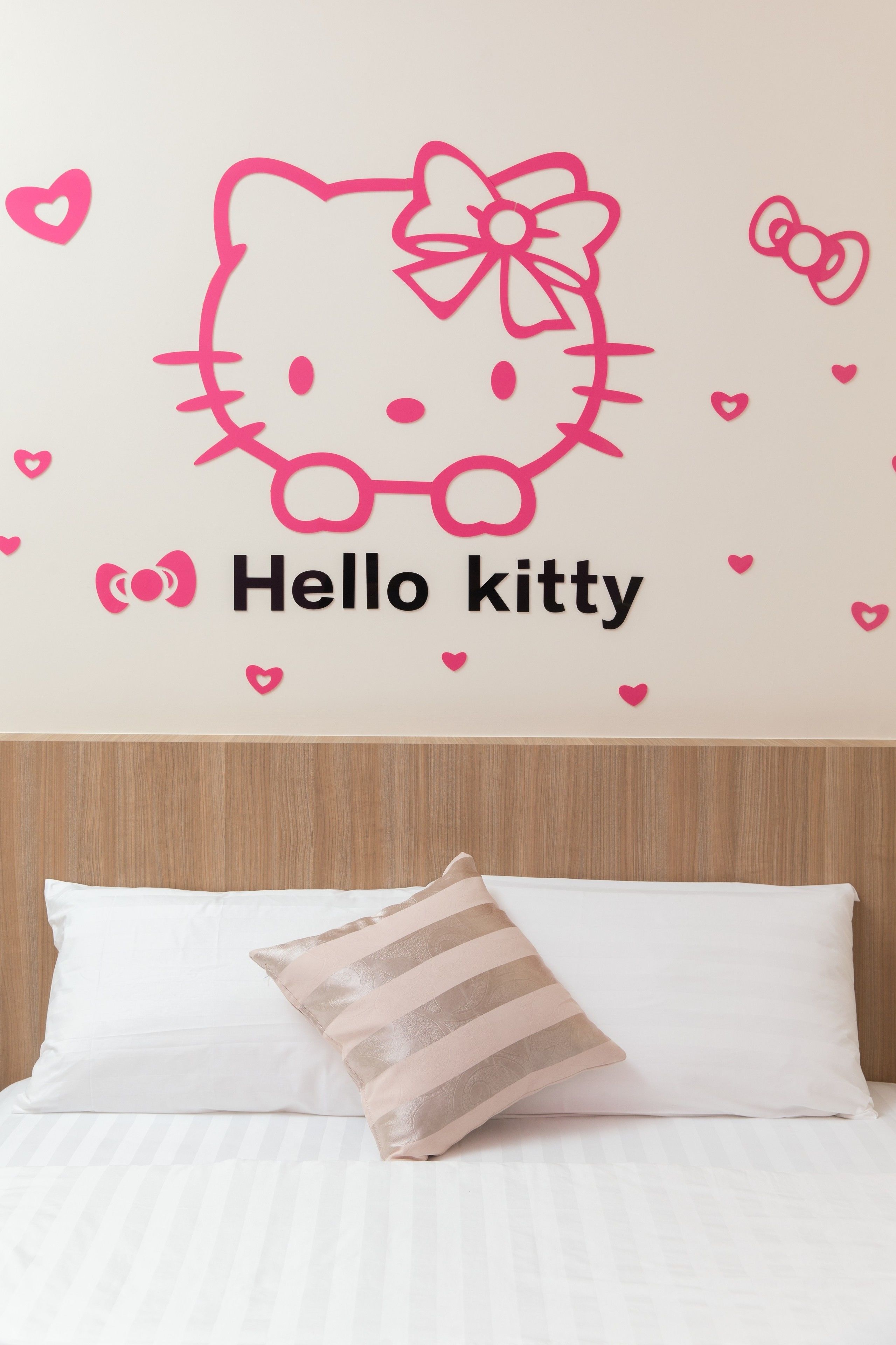 A bedroom with a bed, a pillow, and a wall decal of Hello Kitty.