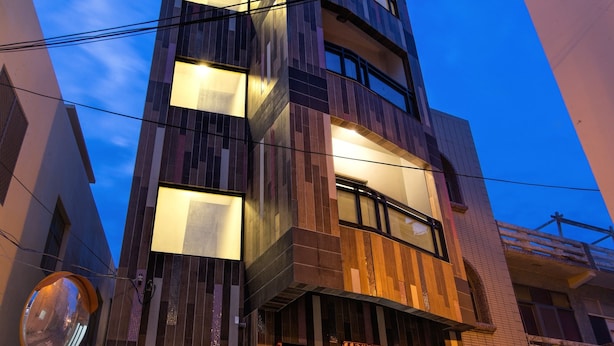 Un hôtel à plusieurs étages au design moderne, doté d’une entrée imposante avec des portes en verre et d’un ascenseur bien visible.
