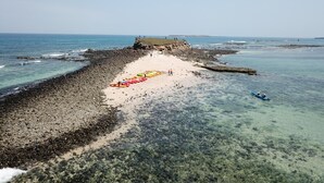Une zone côtière avec une plage rocheuse, des eaux cristallines et un phare visible au loin.