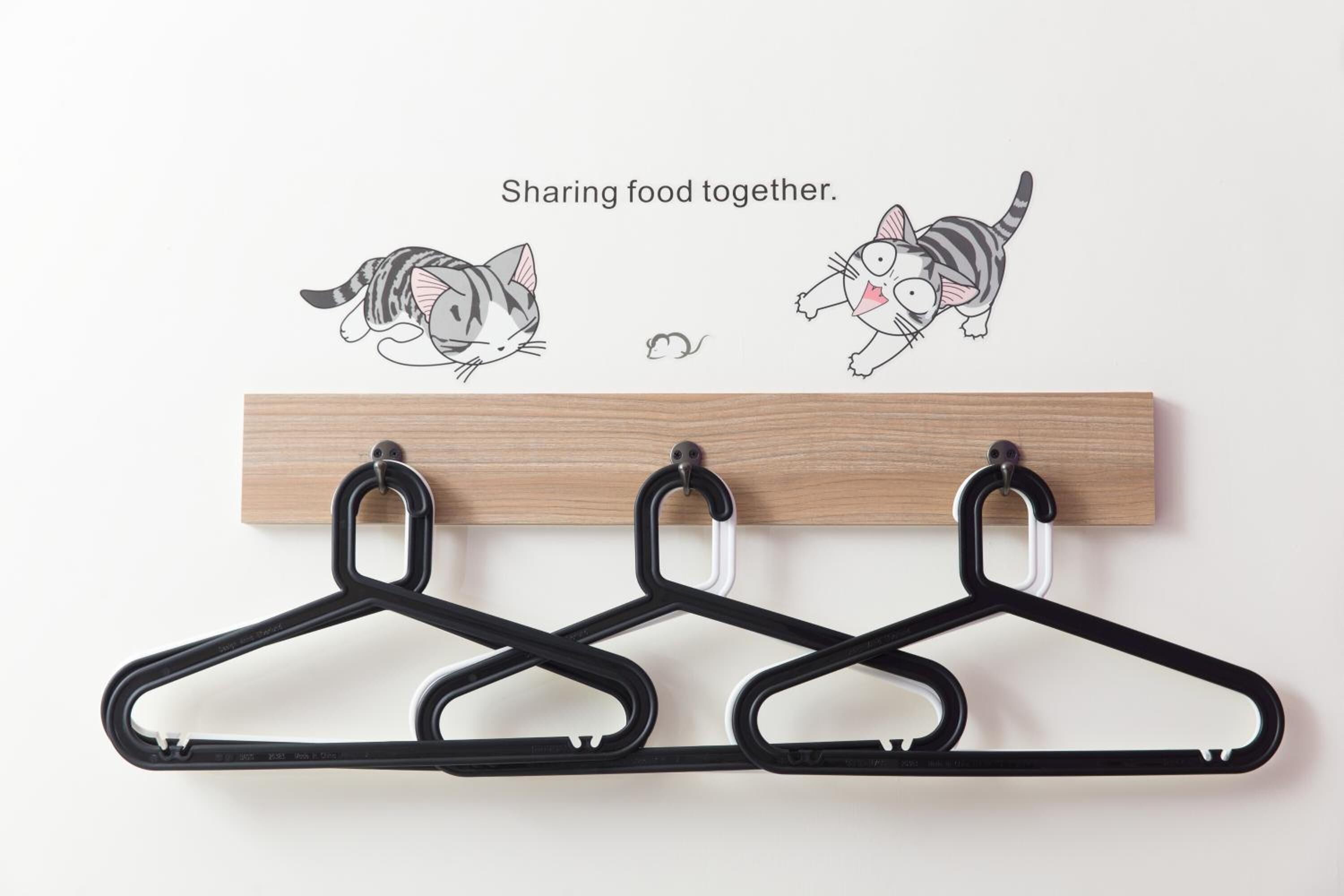Una tabla de madera con cuatro perchas negras e ilustraciones de gatos.