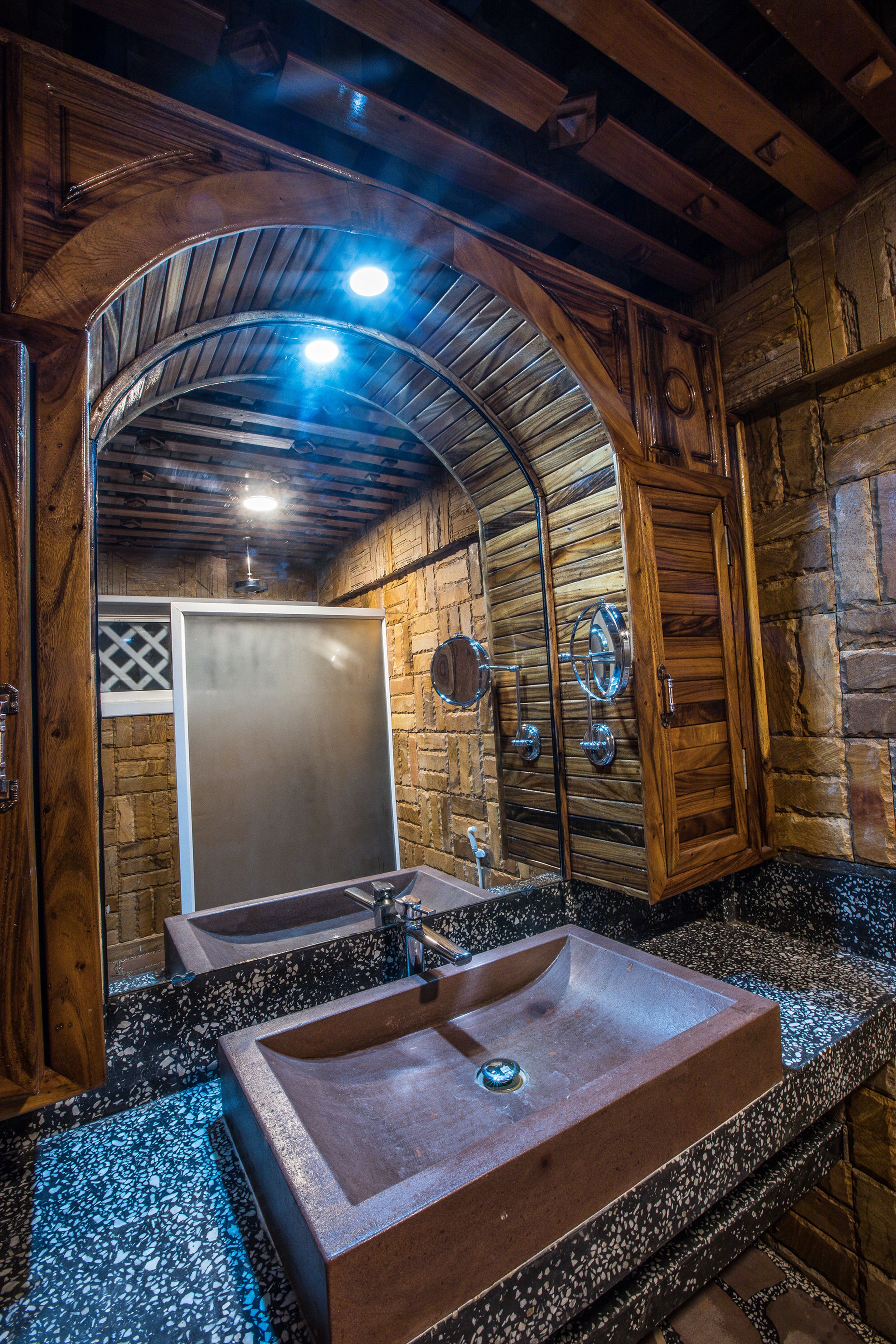 Un baño rústico con un lavabo grande de piedra, vigas de madera y una pared de piedra.