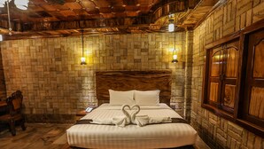A hotel room with a brick-patterned wall, a wooden headboard, and a bed with white linens and a heart-shaped towel arrangement.