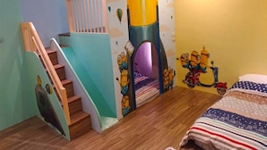 Une chambre d’enfant avec une fresque murale sur le thème de l’espace, un escalier en bois et un lit recouvert d’une couverture à motifs.