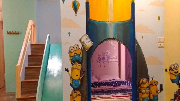 Un espace de jeux pour enfants comprenant un toboggan, un mur d’escalade et une structure en forme de tente décorée aux couleurs des personnages de « Moi, moche et méchant ».