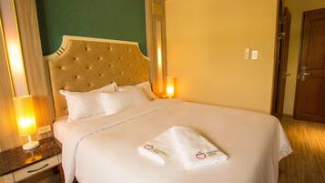A hotel room with a large bed, two bedside lamps, a wooden nightstand, and a door.