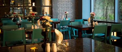 Un ristorante con sedie color acquamarina, un bancone in marmo e una parete decorativa con motivi geometrici.