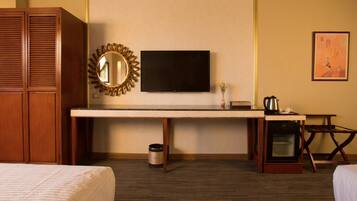 Habitación de hotel con cama, escritorio con televisor, cafetera, microondas y horno pequeño.