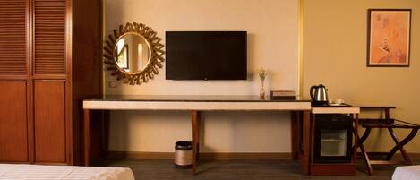 Habitación de hotel con cama, escritorio con televisor, cafetera, microondas y horno pequeño.