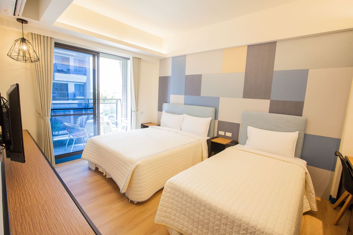 Habitación de hotel con dos camas, televisión, balcón con una silla y vista a la ciudad.