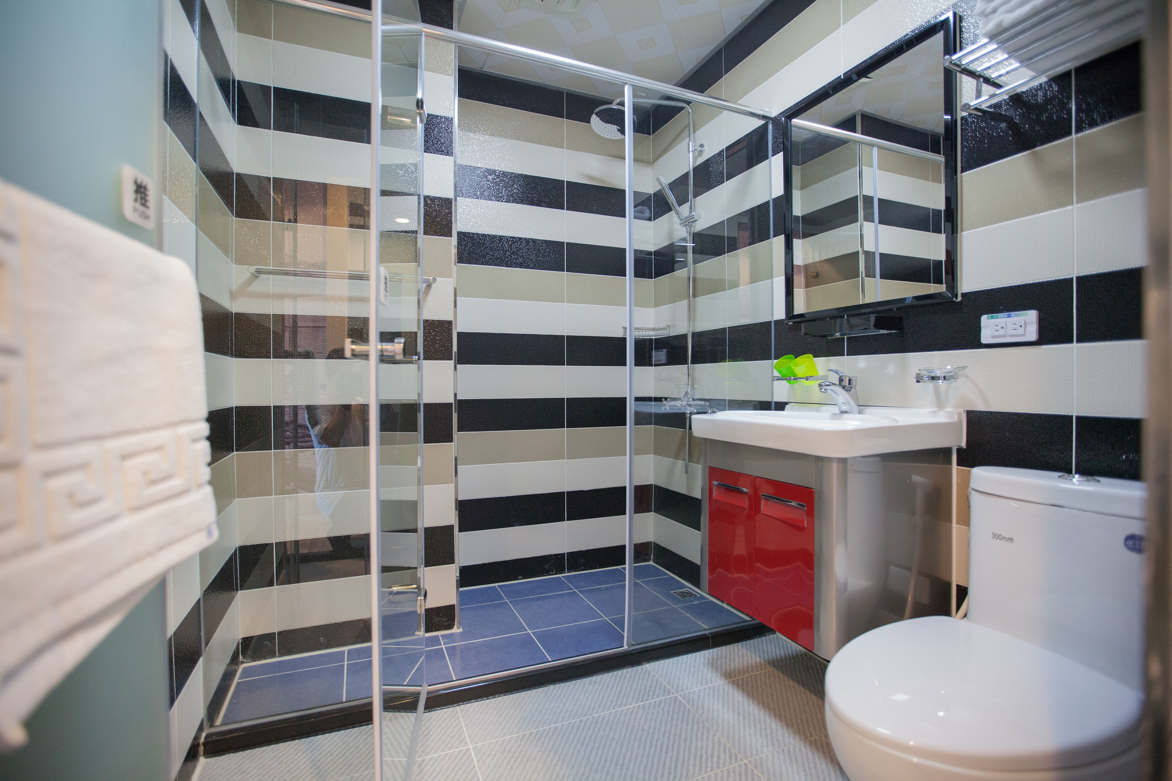 A bathroom with a glass-enclosed shower, a red cabinet, and a white toilet.