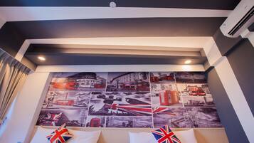 A hotel room with a large wall mural of London landmarks, a bed with two pillows featuring the Union Jack, and an air conditioning unit mounted on the wall.