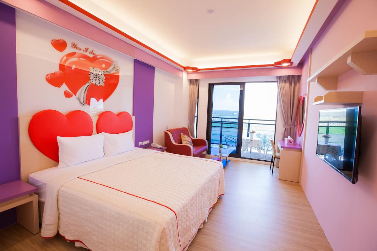 Habitación de hotel moderna con una cama grande, televisor, escritorio y balcón con vistas.