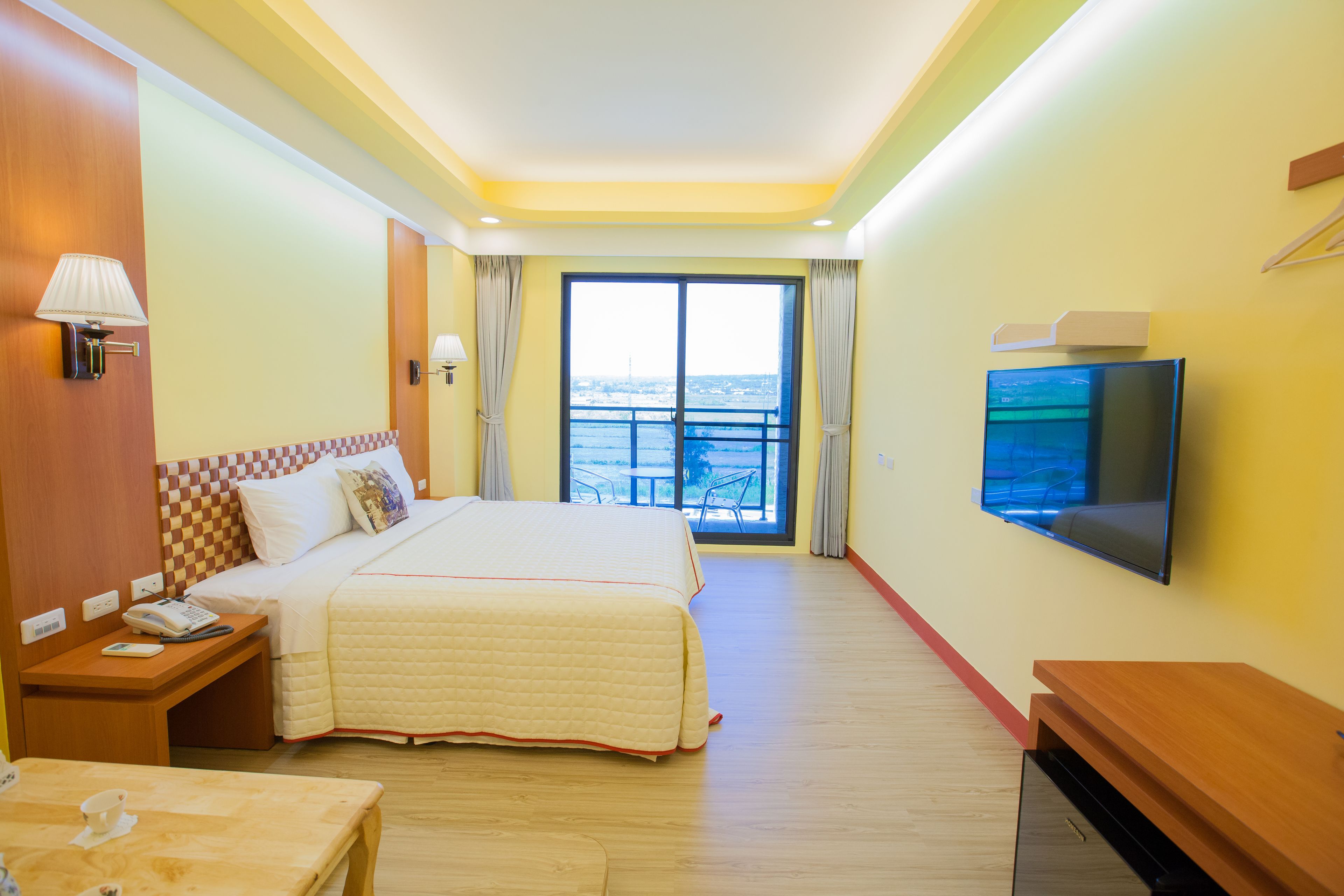 A hotel room with a large bed, a TV, a desk, and a balcony with a view.