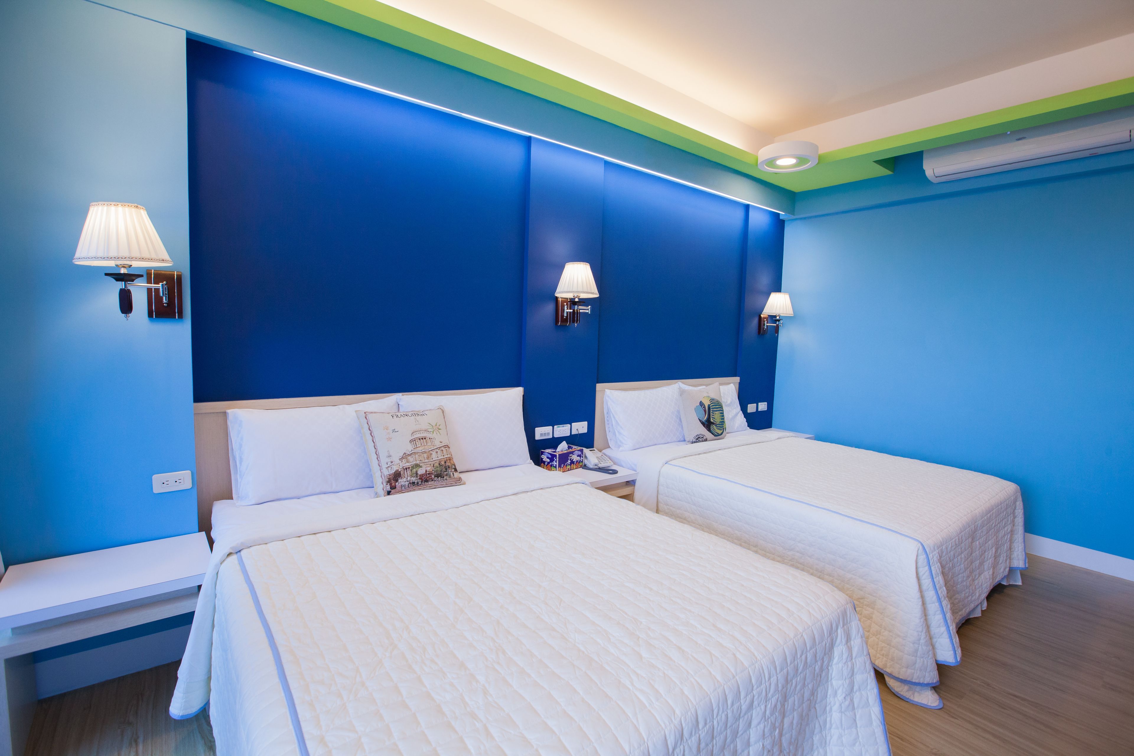 A hotel room with two beds, a nightstand, and a wall-mounted lamp.