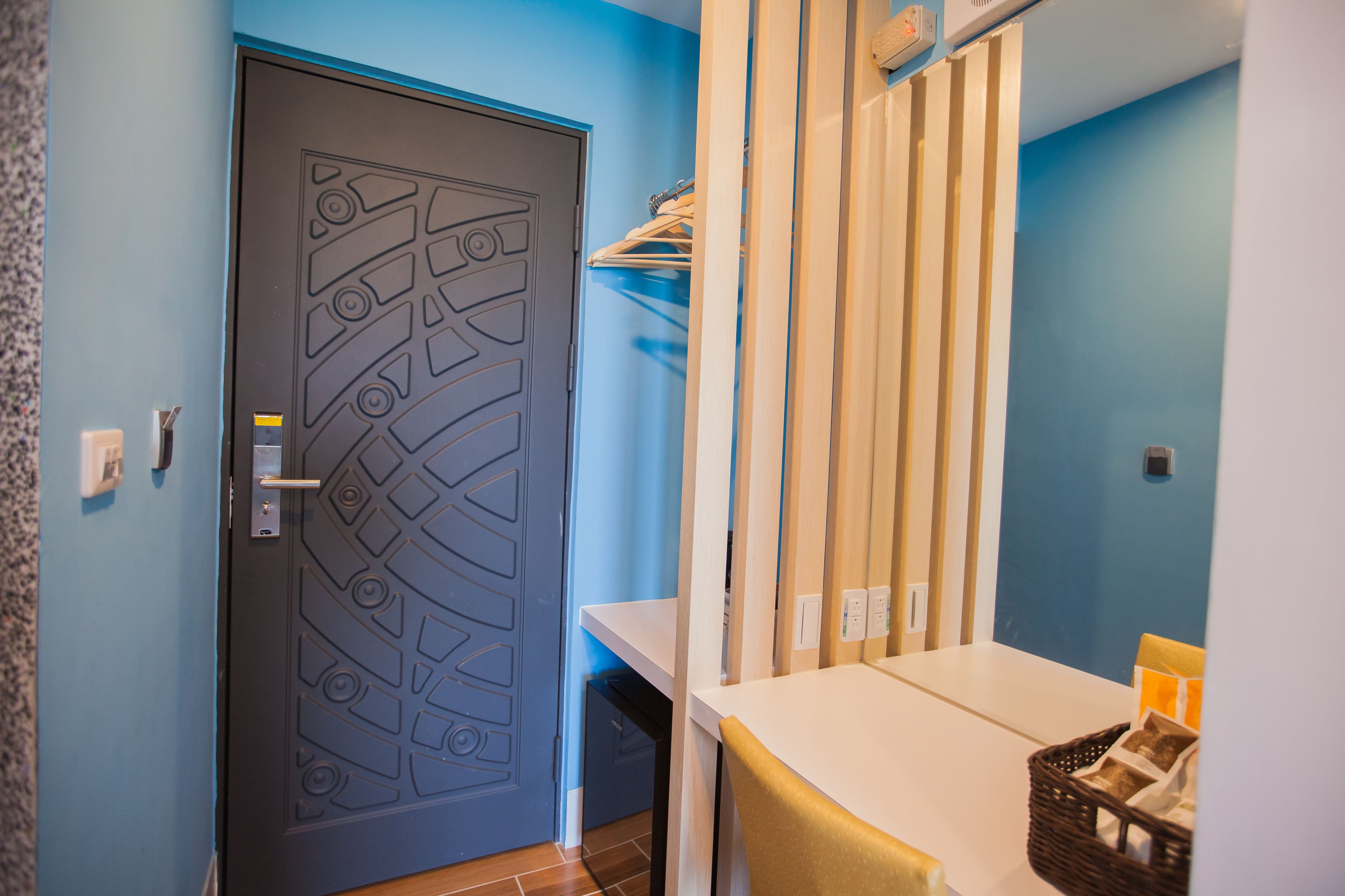 A room with a door featuring a geometric pattern, a white table with a basket, and a blue wall.